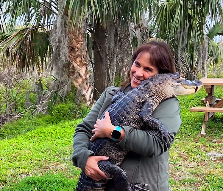 A smiling woman holds an alligator outdoors, from the Fran&rsquo;s Adventures column